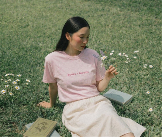 Woman sitting on grass reading a book with flowers around her