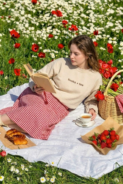 Woman reading a book in a field of flowers with a picnic setup.