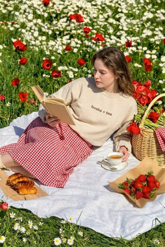 Woman reading a book in a field of flowers with a picnic setup.