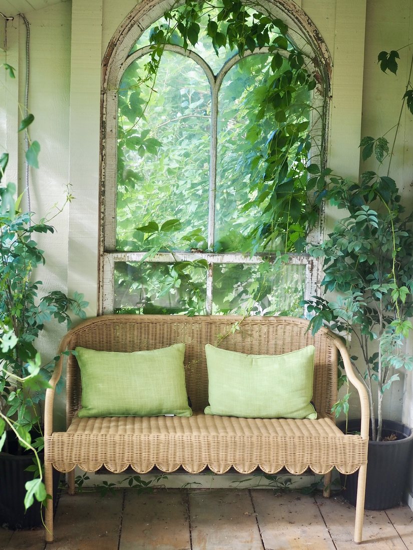 A wicker porch bench with green pillows at Nottawa Cottage Bookstore
